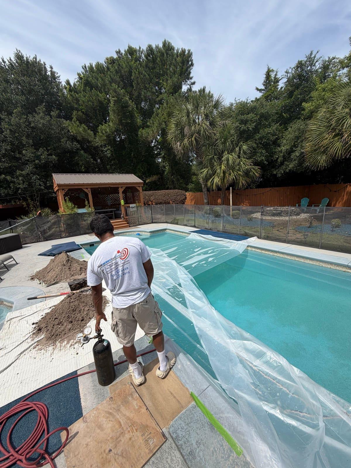 A technician beside a sheeted-over pool with a pressure-test cylinder, sand piles on the deck