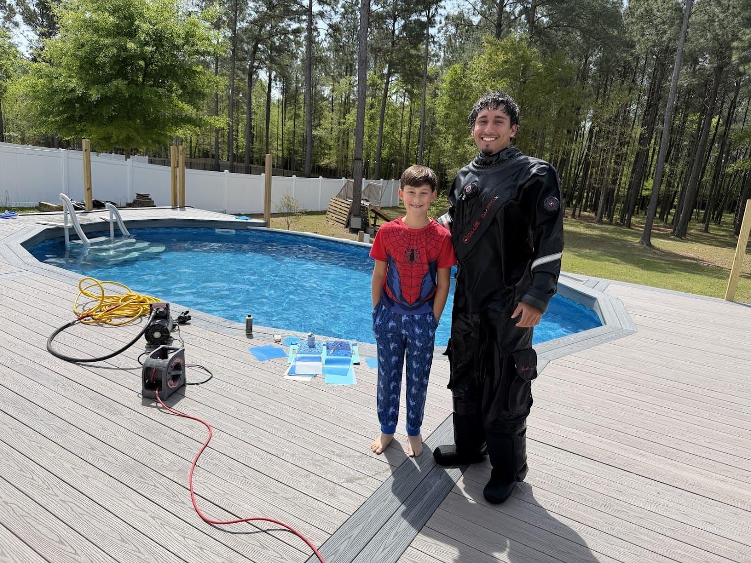 Leak-detection technician in a drysuit beside a residential pool with professional equipment on the deck.